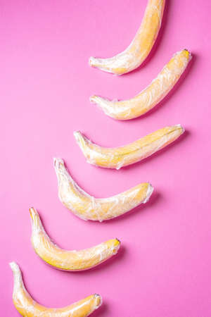 Banana fruit wrapped in stretch wrap plastic on pink background, minimalistic creative layout, ecology and environment conceptの写真素材