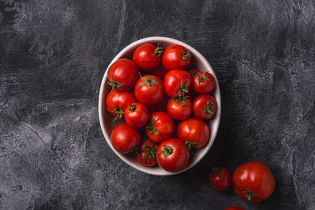 Fresh ripe tomatoes in bowl on dark concrete background, top viewの写真素材