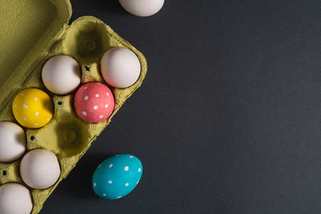 Colorful polka dot Easter eggs in egg tray on dark background, greeting card