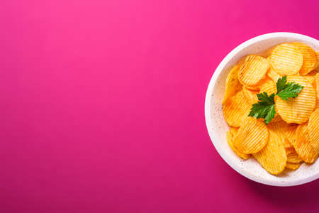 Fried corrugated golden potato chips with parsley leaf in wooden bowl on pink background, top view copy spaceの写真素材