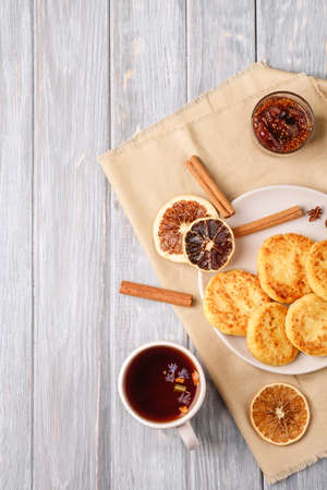 Cottage cheese fritters with hot black aromatic tea, Christmas breakfast mood with anise, cinnamon and dried citrus on wooden background, top viewの写真素材