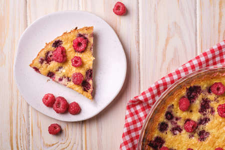 Sweet tasty pie with jellied and fresh raspberry fruits in baking dish and plate with red tablecloth towel, wooden table background, top viewの写真素材