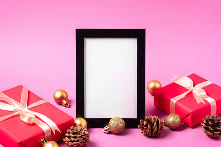 Christmas minimal composition with empty picture frame. Golden ornament, gift boxes and pine cones decorations. Mock up greetings card templateの写真素材