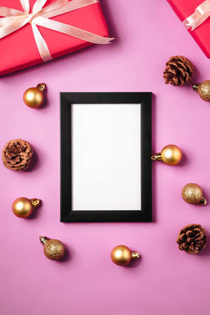 Christmas minimal composition with empty picture frame. Golden ornament, gift boxes and pine cones...