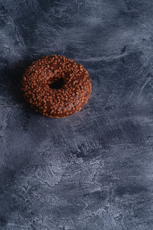 Chocolate donut with sprinkles, sweet glazed dessert food on dark concrete textured background, angle view copy spaceの写真素材