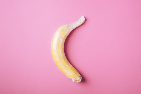 Banana fruit wrapped in stretch plastic on pink backgroundの写真素材