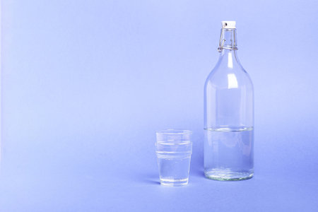 Glass with water near to bottle on blue background