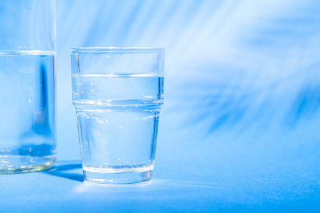 Glass with water near to bottle on blue background