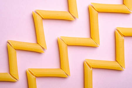 Italian pasta, raw penne tube macaroni zigzag pattern on pink background, top view, abstract foodの写真素材