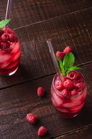 Fresh ice cold berry juice drink with mint, summer raspberry lemonade in two glass with straws on brown wooden background, angle view selective focusの写真素材