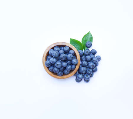 Blueberries on bowl white background. Some berries and green leaves around. Top view.