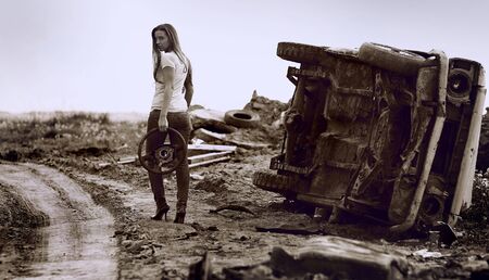 The girl with wheel in a hand against broken car. Photo.の写真素材