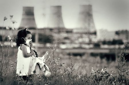 Innocent child in a respiratory mask with a doll in her hands walking against power station polluting air. Ecological theme.の写真素材