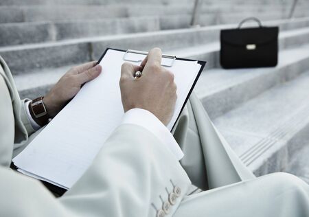 male business executive sitting on stairs and do marks on sheetsの写真素材