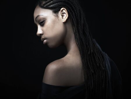 Portrait of a beautiful young black woman posing in black background.の写真素材