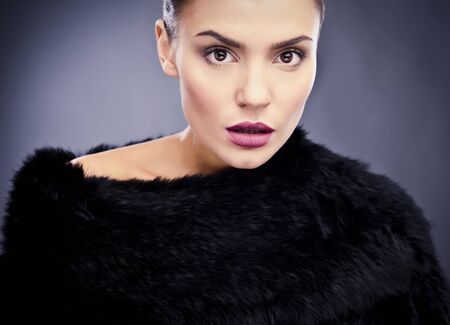 Close-up face portrait of stylish fashionable pretty woman in fur against grey background  の写真素材