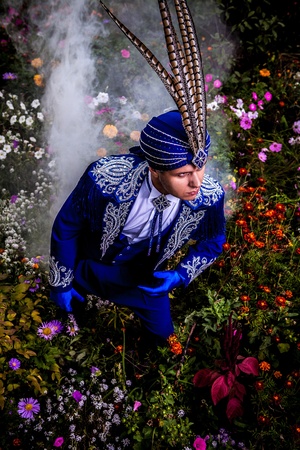 Man in expensive dark blue suit of illusionist pose on flower meadow  