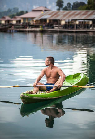 Strong young man in kayak on the picturesque lake in Thailand 