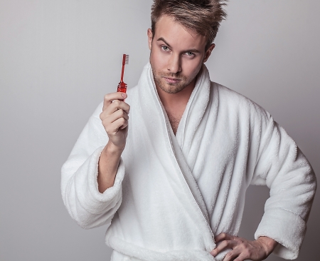 Beautiful adult man on white bathrobe brushing teeth   の写真素材
