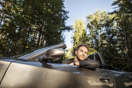 Elegant young happy man in convertible car outdoor   