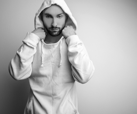 Studio portrait of young handsome man in white sweater with hood. Blackwhite photo.の写真素材