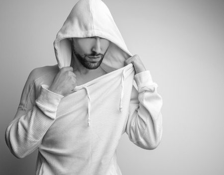 Studio portrait of young handsome man in white sweater with hood. Blackwhite photo.の写真素材
