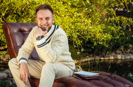Young handsome man in sit in luxury sofa with iPad in summer garden.