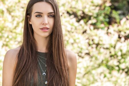 Outdoors portrait of beautiful young woman in casual green dress posing in summer garden.の写真素材
