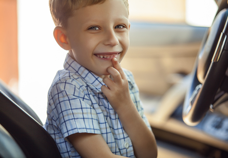 Outdoor portrait of happy blond little boy who explore salon of sport auto.