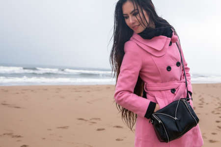 Portrait of attractive young woman with long beautiful hairs dressed pink coat, which posing in autumn North sea beach.の写真素材