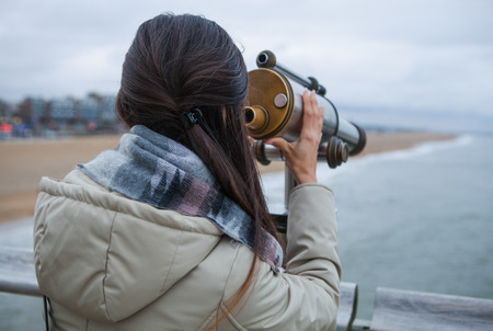 Beautiful young woman with magnificent hairs near telescope on pier in the Hague.の写真素材