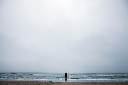 Young woman with long hair standing back on beach of the North Sea in cloudy evening.の写真素材