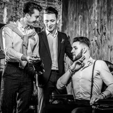 Three young elegant positive friends pose in interior of barbershop. Black-white photo.