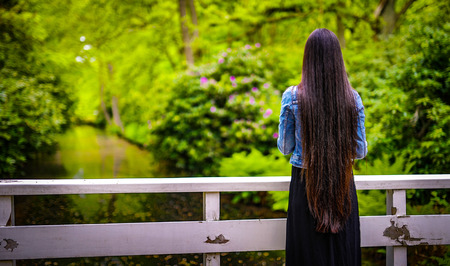 Long-haired girl standing with her back looking at a blooming summer park.の写真素材