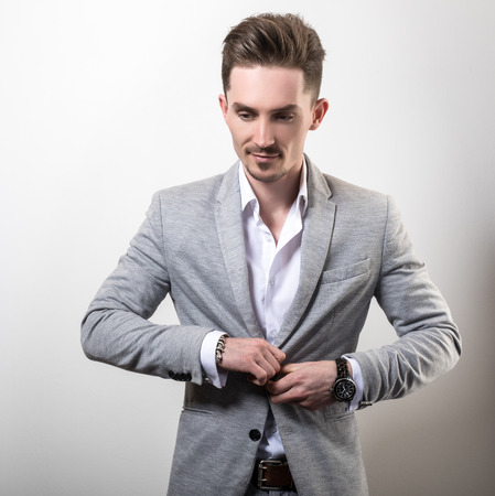 Handsome young elegant man in grey jacket pose against studio background.の写真素材