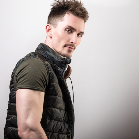 Handsome friendly sporty man in green t-shirt listening music against gray studio background.の写真素材