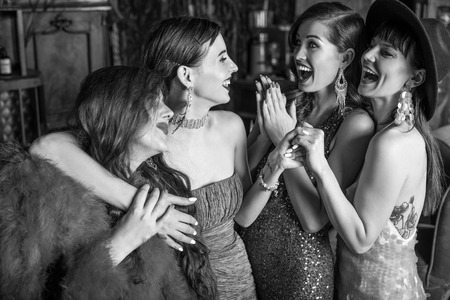 Group of young laughing stylish girls dressed classical style in interior of luxury club. Black-white photo.の写真素材