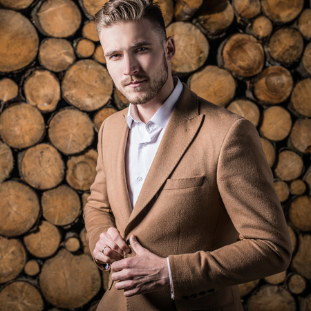 Portrait of young beautiful fashionable man in coat against wooden background.の写真素材