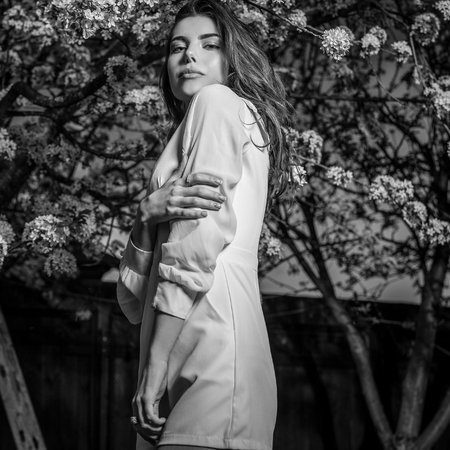 Portrait of beautiful young woman in autumn garden against blooming cherry. Black-white photo.の写真素材