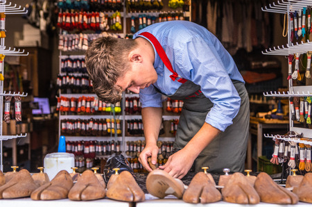 PRAGUE, CZECH REPUBLIC - OCTOBER 21, 2018: Young master repairs shoes in window of taking orders.のeditorial素材