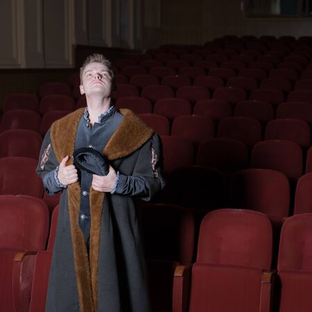 Actor dressed historical costume in interior of old theater.