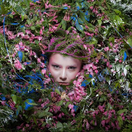 Female portrait in fairy tale stylisation surrounded with natural plants and flowers.