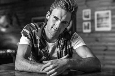 Handsome young man in in casual clothes pose against house interior. Black-white portrait.