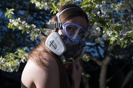 Young beautiful girl portrait in a mask with degree of protection posing in twilight of spring garden.の写真素材