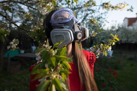 Young beautiful girl portrait in a mask with degree of protection posing in twilight of spring garden.の写真素材