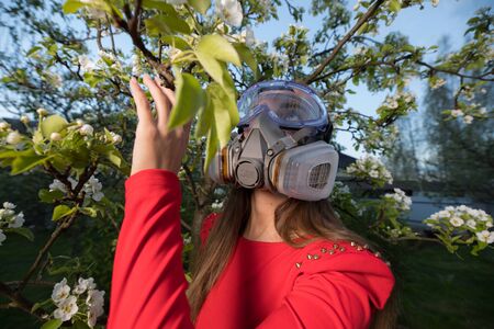 Young beautiful girl portrait in a mask with degree of protection posing in twilight of spring garden.の写真素材