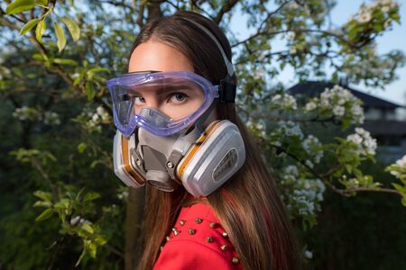 Young beautiful girl portrait in a mask with degree of protection posing in twilight of spring garden.の写真素材