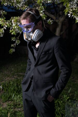 Young man portrait in mask with degree of protection posing in twilight of spring garden.の写真素材