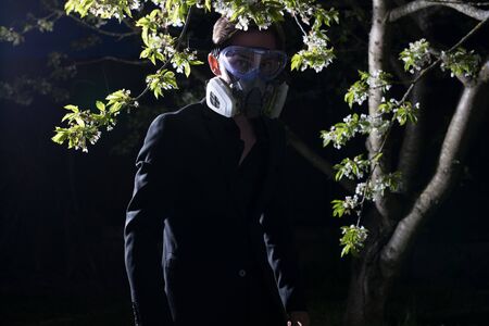 Young man portrait in mask with degree of protection posing in twilight of spring garden.の写真素材