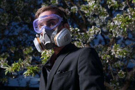 Young man portrait in mask with degree of protection posing in twilight of spring garden.の写真素材